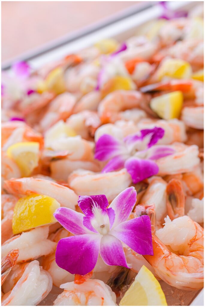 Close-up of shrimp garnished with lemon wedges and purple flowers.