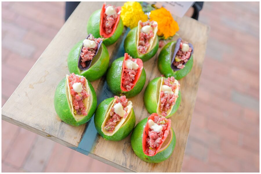 Small tacos served inside halved limes on a tray, garnished with marigold flowers.