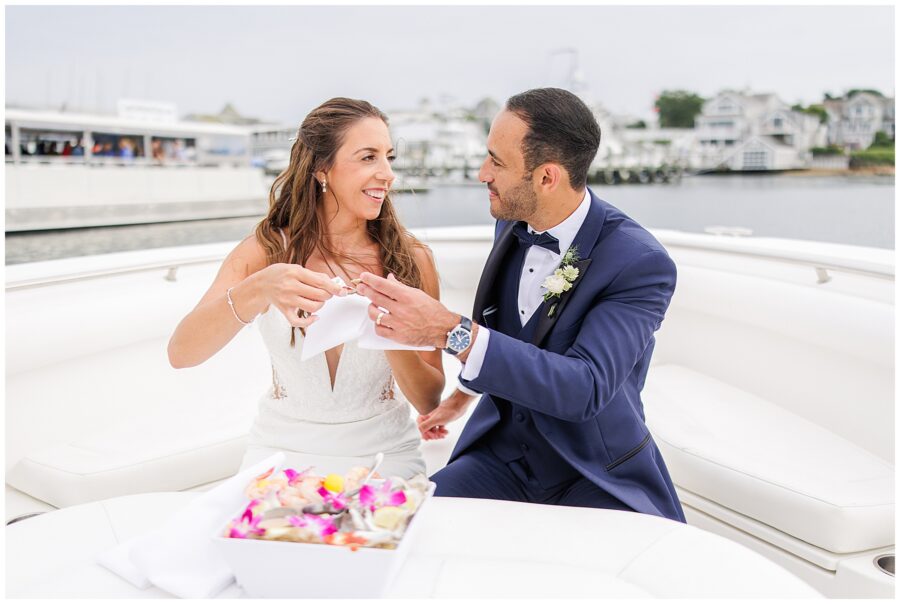 Bride and groom sitting on a boat, enjoying shrimp cocktail, with water and docks in the background.