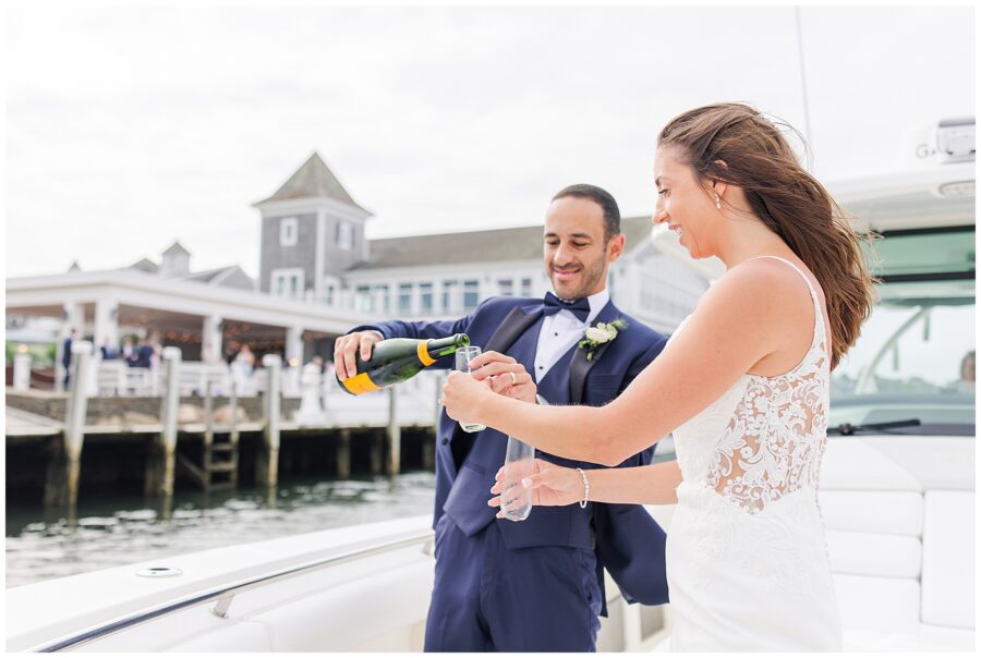 Groom pouring champagne into glasses on a boat while the bride holds one glass.