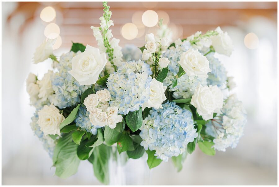 Floral arrangement with white roses and blue hydrangeas, with blurred lights in the background.