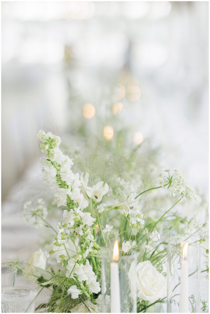 Close-up of white flowers and greenery with candles at a wedding reception.