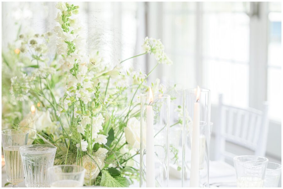 Elegant table centerpiece with white flowers and lit candles at a wedding.