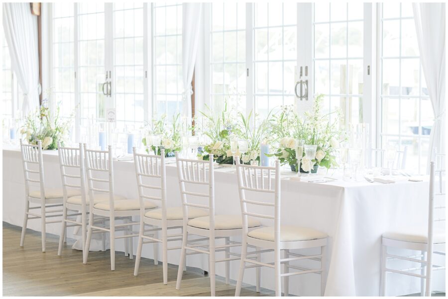 Long table with white chairs and floral arrangements at a wedding in Wychmere Beach Club.