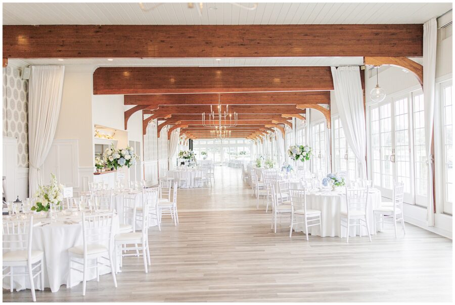 Harbor Room at Wychmere Beach Club with wooden beams, white chairs, and floral centerpieces at a wedding.