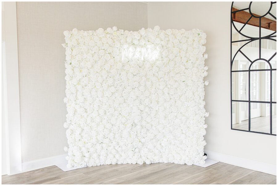 White flower wall backdrop with “Mr & Mrs” in neon lights at a wedding.