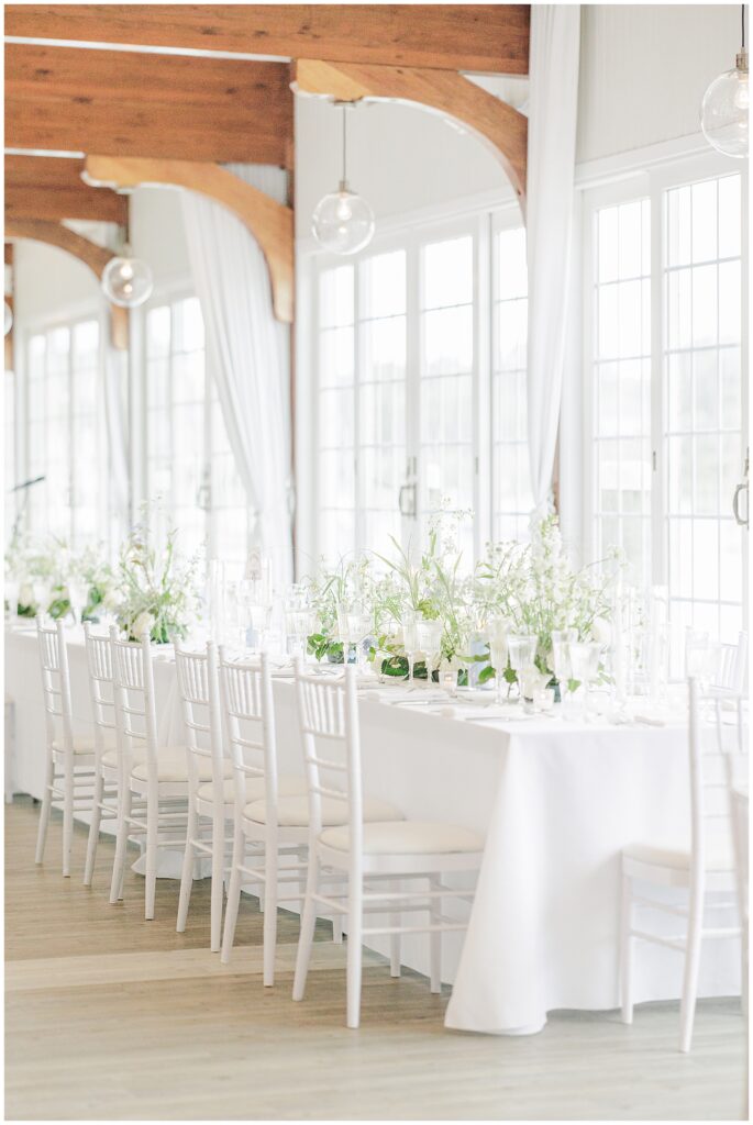 Long table with white floral arrangements and greenery at a wedding reception.