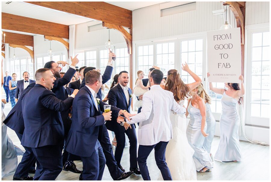 Bride and groom celebrate with wedding party. "From Good to Fab" sign visible as they dance and cheer.