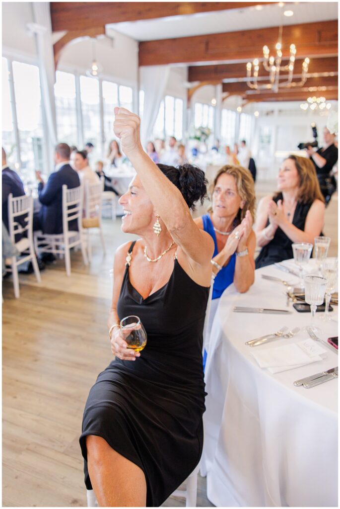 Wedding guest raising her glass in a toast, smiling joyfully at a reception table.