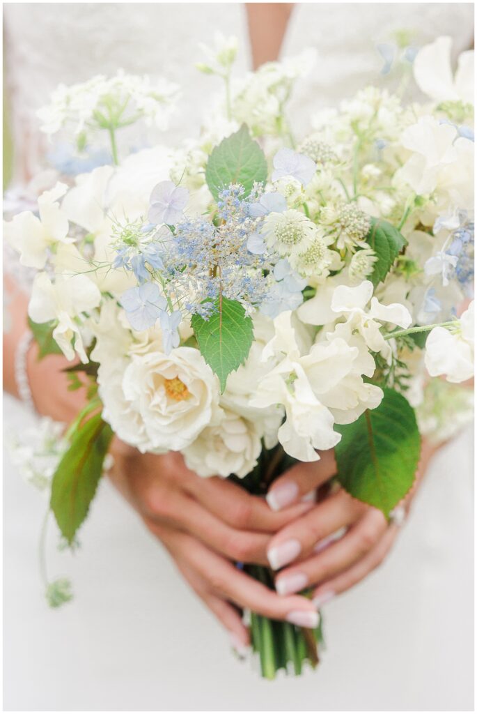 Close-up of bride's bouquet with white and light blue flowers. Delicate floral arrangement for beach wedding.