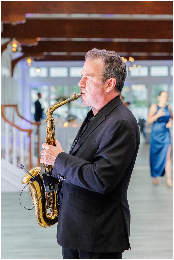 Saxophonist playing at Cape Cod wedding reception. Wooden beams and string lights visible overhead.