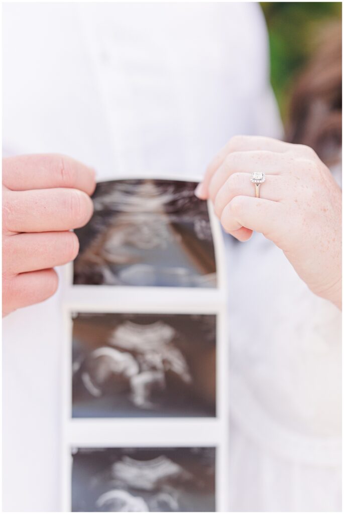 Close-up of couple holding an ultrasound photo, woman’s engagement ring in focus.