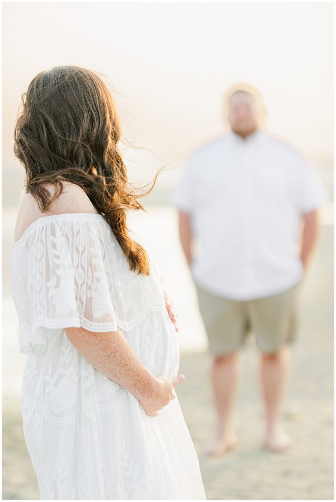 Cape Cod maternity photography featuring a woman looking out at the ocean, partner blurred in the background.