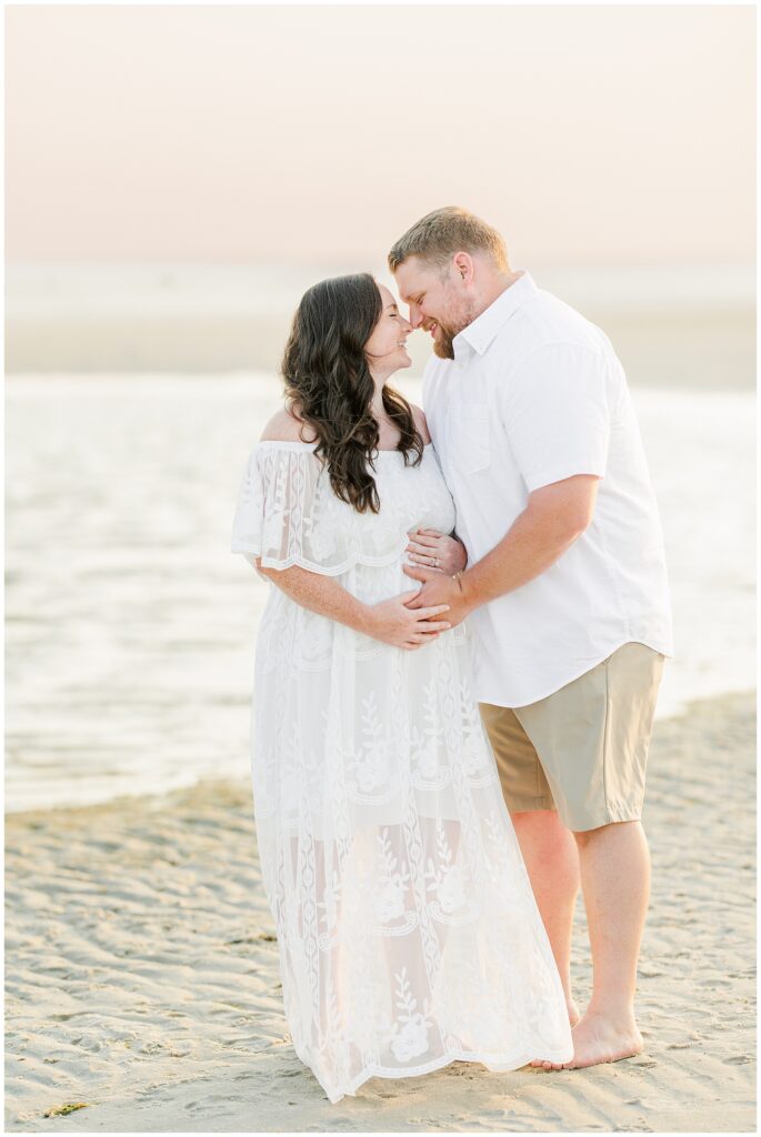 Cape Cod maternity photography of couple on the beach, heads touching, smiling as they cradle her belly.