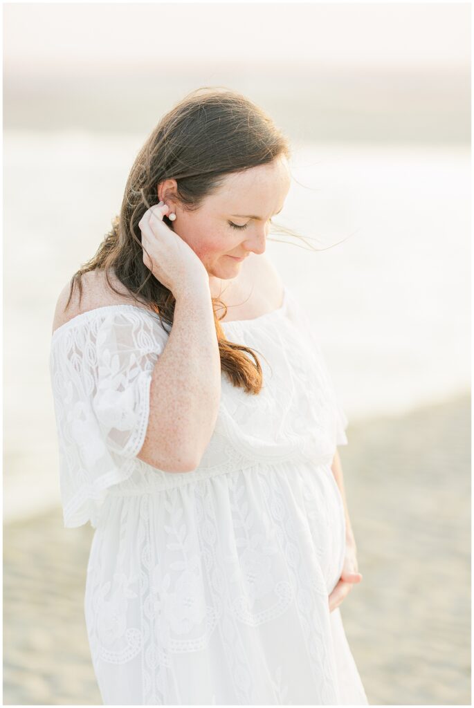 Cape Cod maternity photography of a pregnant woman looking down, holding her belly, with the ocean in the background.