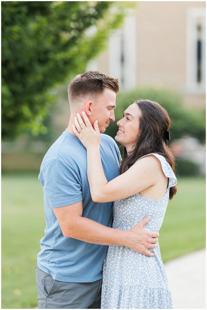 A couple stands together on a tree-lined path, looking at each other affectionately, taken by a  Massachusetts photographer.
