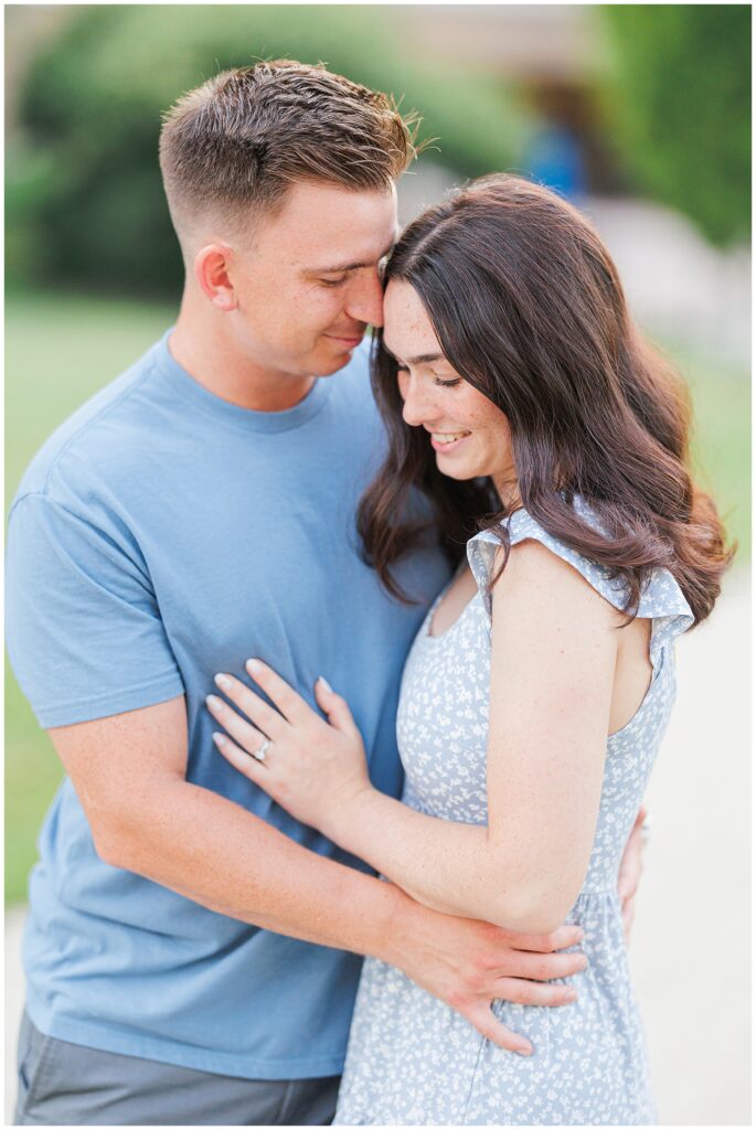 A couple stands closely together, both smiling with eyes closed, as the man wraps his arms around the woman from behind during an anniversary shoot with a Massachusetts photographer.