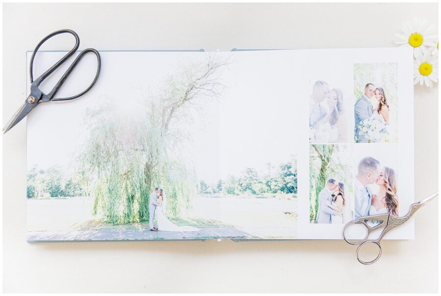 Open wedding album displaying a page with photos of the couple, with scissors and daisies nearby.