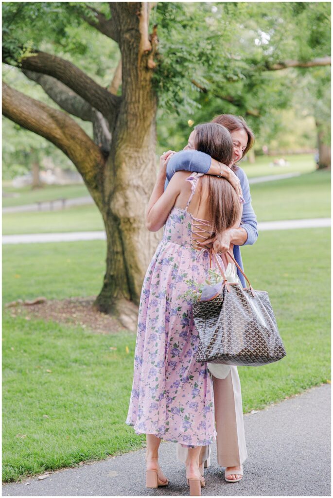 A couple embraces their family after the proposal in Boston Public Garden. The woman hugs another woman.