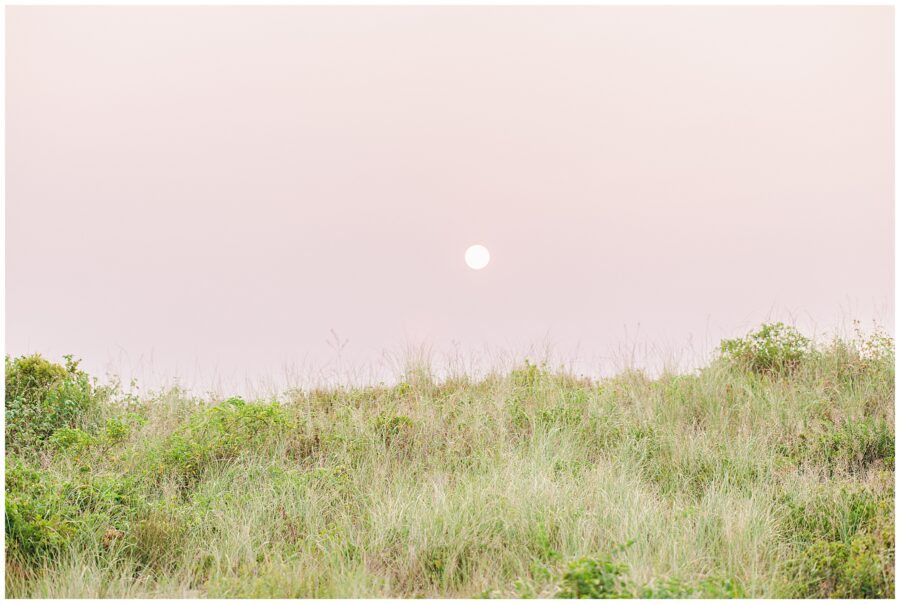 The sun sets over a grassy dune at Great Island Trail, casting a warm, soft light over the landscape, perfect for capturing serene maternity moments.