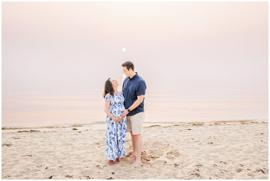 A couple stands barefoot on the sandy beach at Great Island Trail, Wellfleet, MA, as the sun sets in the background. The tranquil scene is ideal for Cape Cod maternity photographers to capture stunning, peaceful images.