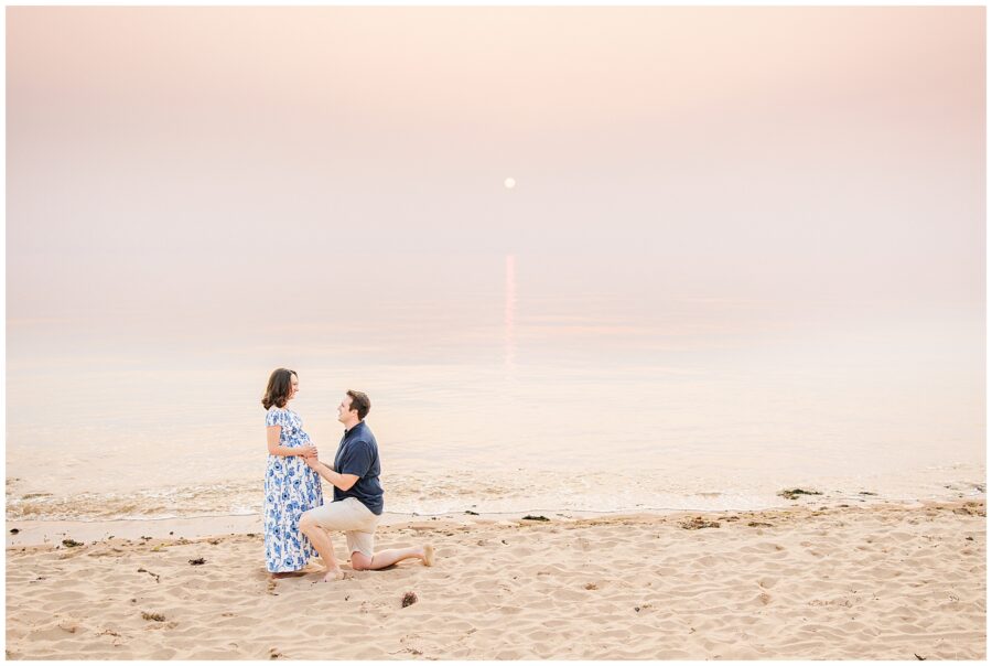 The man kneels in front of the pregnant woman on the beach, gently holding her belly as the sun sets behind them. The serene backdrop of Great Island Trail makes this a special moment for any Cape Cod maternity photographer to capture.