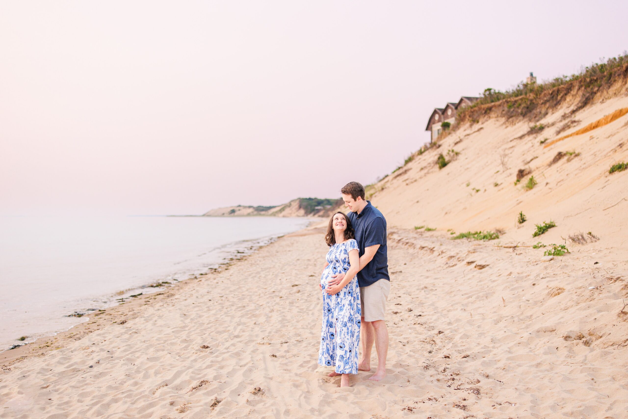 The couple stands on the sandy beach at Great Island Trail, with the dunes rising behind them and the peaceful ocean stretching into the distance. This quiet and beautiful location is perfect for Cape Cod maternity photography.