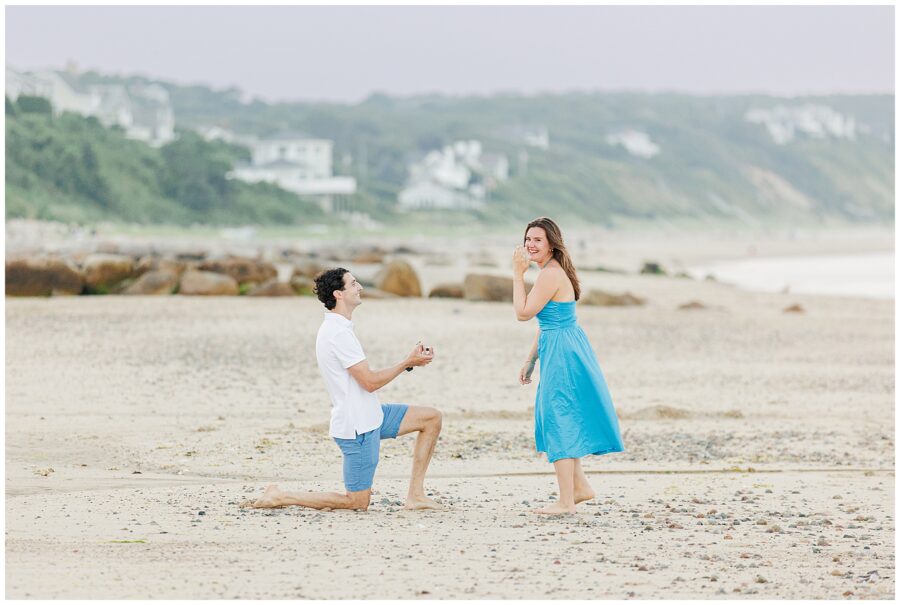 The man proposes, while the woman smiles in joy on the beach at Sandwich, MA.