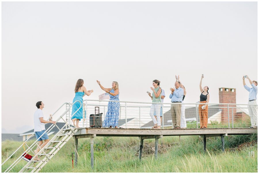 Family and friends clap and cheer from a deck in Sandwich, MA, celebrating the proposal.