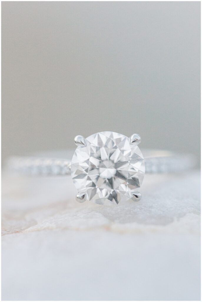 Close-up of a large diamond engagement ring on a simple band, resting on a light-colored surface.