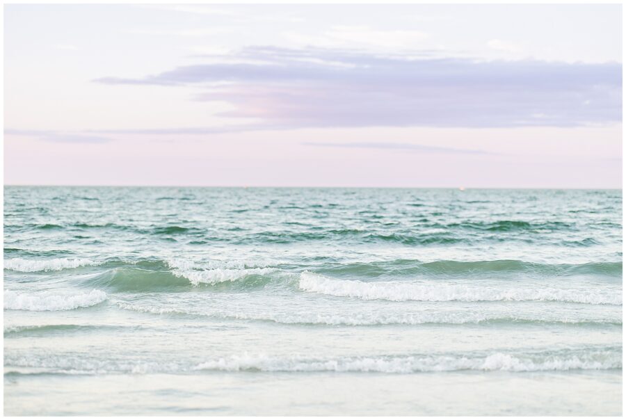 Calm ocean waves gently roll toward the shore under a pastel sky.