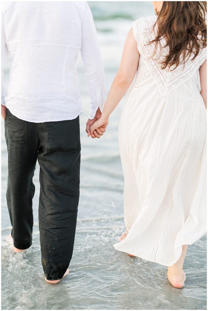 A close-up of the couple holding hands as they walk barefoot in the shallow water.