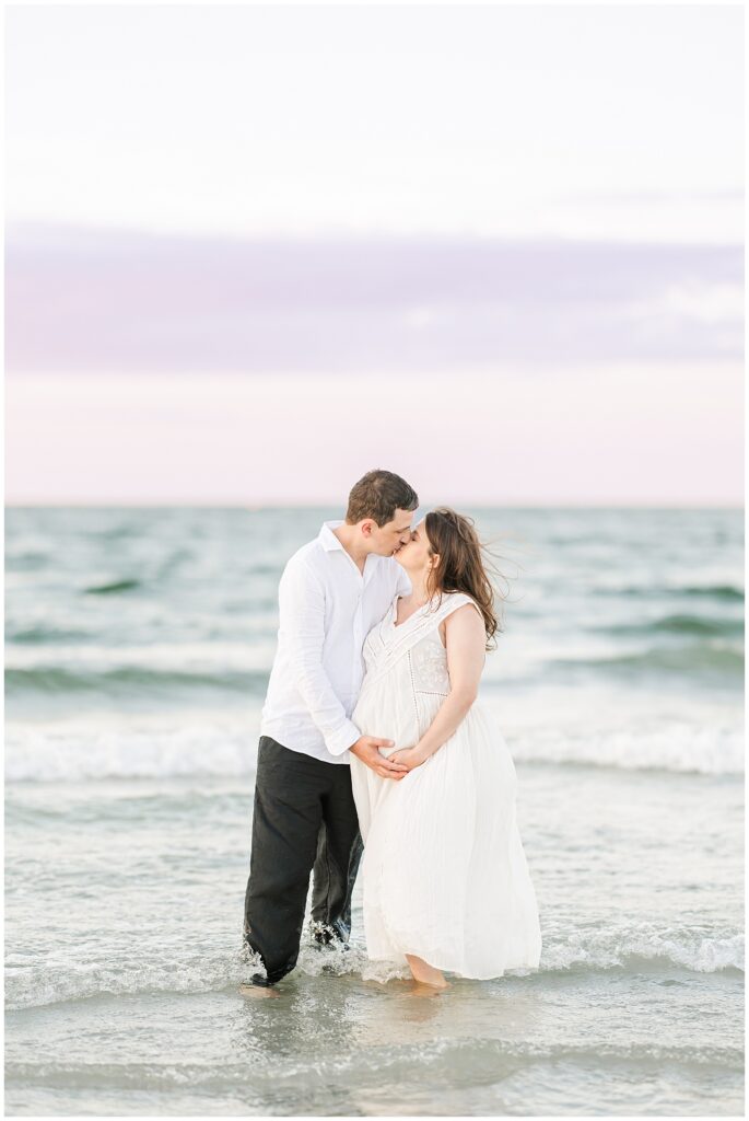 The couple shares a kiss in the water, the man holding the woman’s belly as gentle waves surround them.