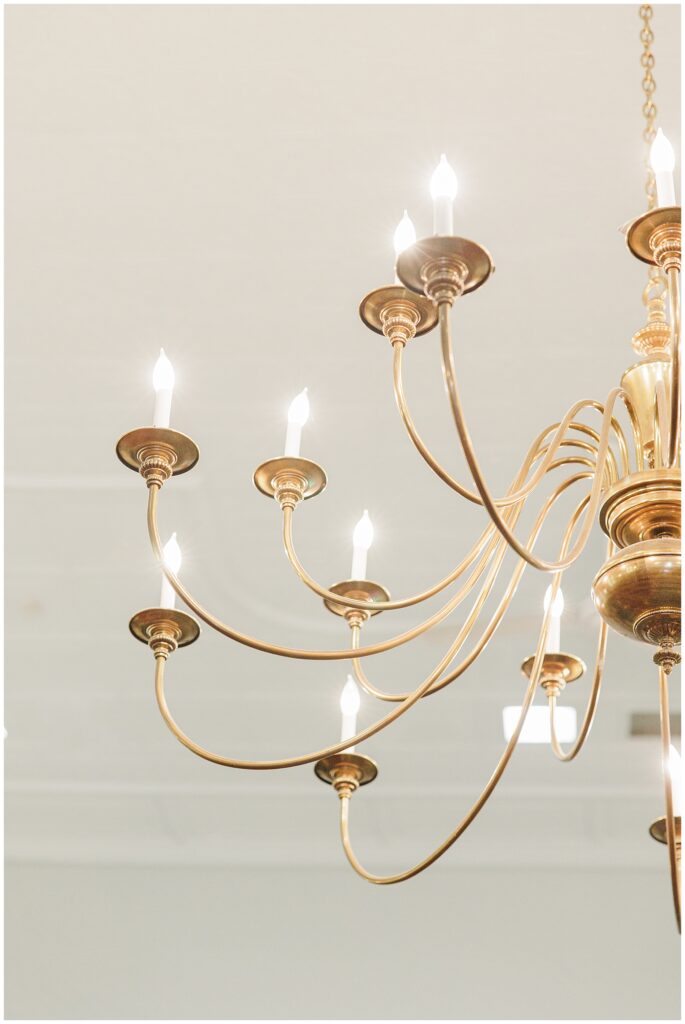 A close-up of a gold chandelier with several lit candles on curving arms.