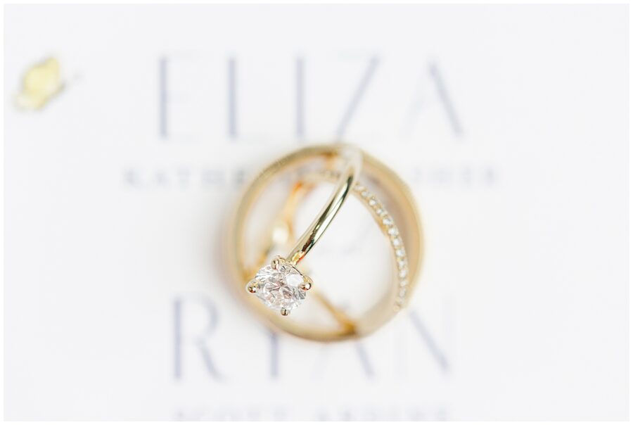 A close-up of a diamond engagement ring and a gold wedding band against the backdrop of the wedding invitation.