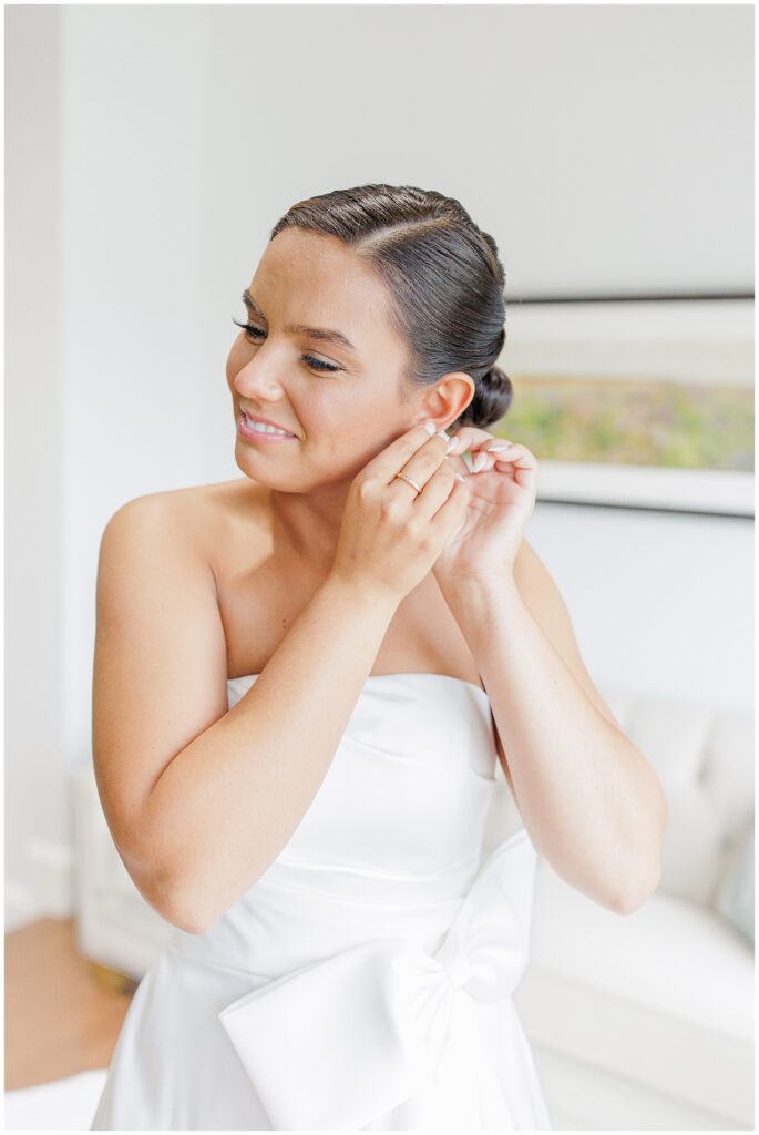 The bride inserting pearl earrings while wearing her strapless white wedding gown.