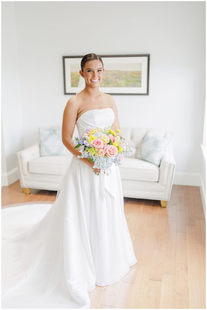 Bride standing in a brightly lit room at Pembroke Pines Country Club, wearing a strapless white gown and holding a colorful bouquet of roses, hydrangeas, and yellow blooms.