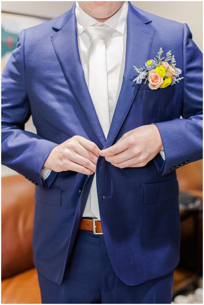 Groom in a navy blue suit with a boutonniere of peach roses and yellow blooms, buttoning his jacket at Pembroke Pines Country Club.