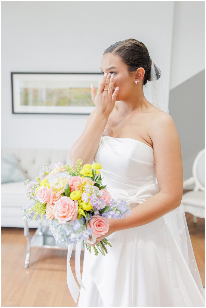 Emotional bride wiping her eye while holding her bouquet, preparing for her first look with her father at Pembroke Pines Country Club.