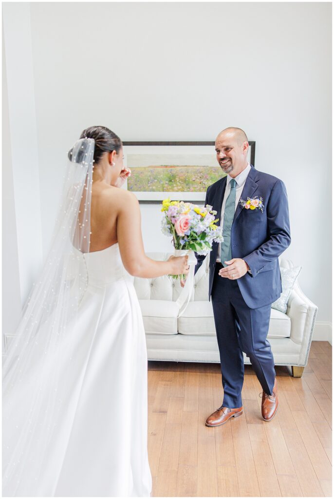 The bride and her father smiling at each other during their first look. The father holds the bride’s bouquet, both standing in a sunlit room at Pembroke Pines Country Club.