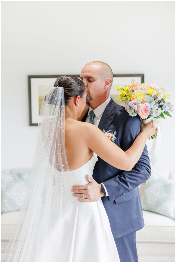 Father kissing his daughter’s forehead while holding her bouquet of pink and yellow flowers at their first look at Pembroke Pines Country Club.