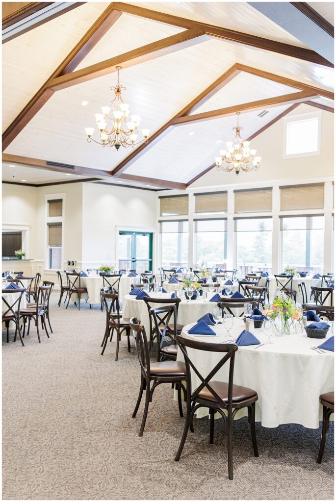 Reception setup at Pembroke Pines Country Club, featuring round tables with floral centerpieces, navy napkins, and large windows bringing in natural light.