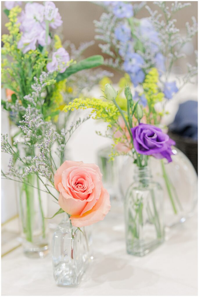 Close-up of reception table floral centerpiece at Pembroke Pines Country Club, showcasing pink and purple roses in small glass vases.