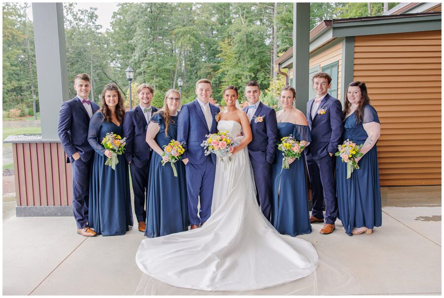 Bride and groom posing with their wedding party on a covered patio at Pembroke Pines Country Club, all dressed in navy blue with matching floral bouquets.