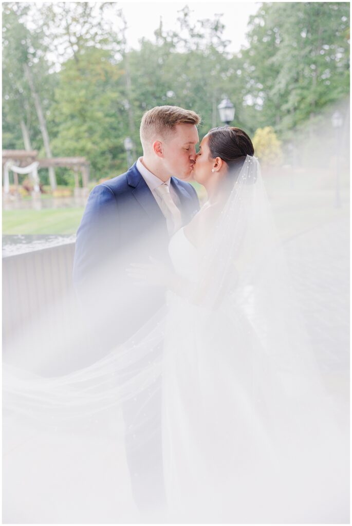 The bride and groom sharing a kiss outside under a flowing veil at Pembroke Pines Country Club in Pembroke, NH.