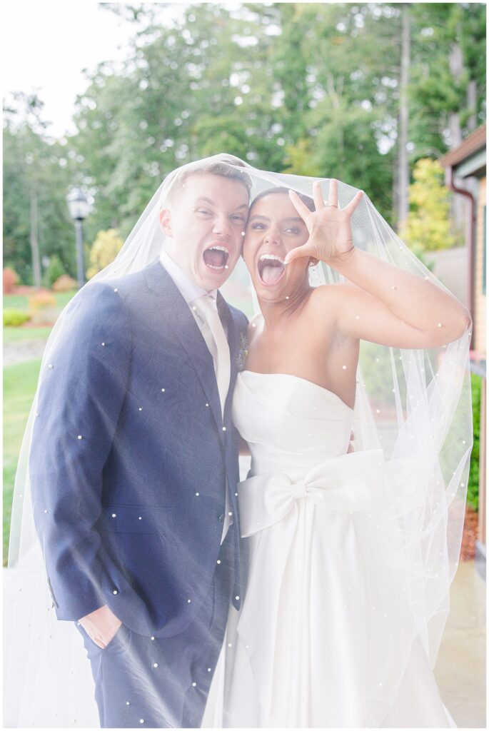 Bride and groom playfully posing under the bride’s veil, making funny faces at the camera at Pembroke Pines Country Club in Pembroke, NH.