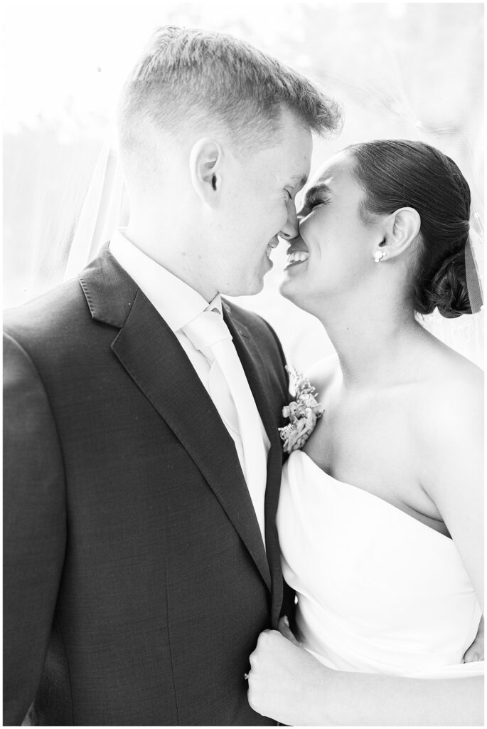 Black-and-white image of the bride and groom with their foreheads touching and smiling at each other under the bride’s veil at Pembroke Pines Country Club in Pembroke, NH.