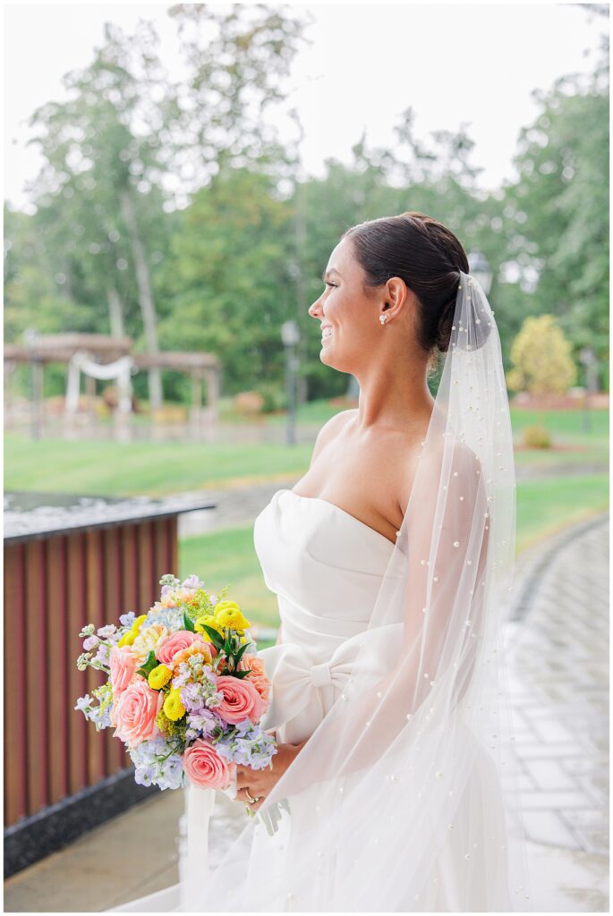 The bride smiling and looking to her left while holding her colorful bouquet under the covered patio at Pembroke Pines Country Club in Pembroke, NH.