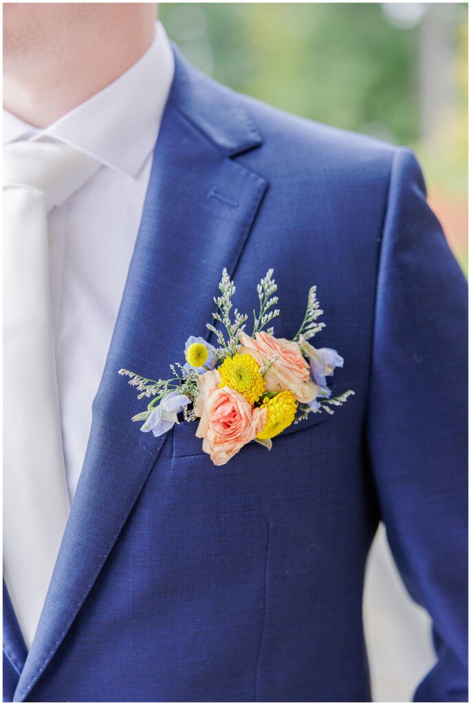 Close-up of the groom’s boutonniere, featuring pink roses, yellow flowers, and greenery, taken at Pembroke Pines Country Club in Pembroke, NH.