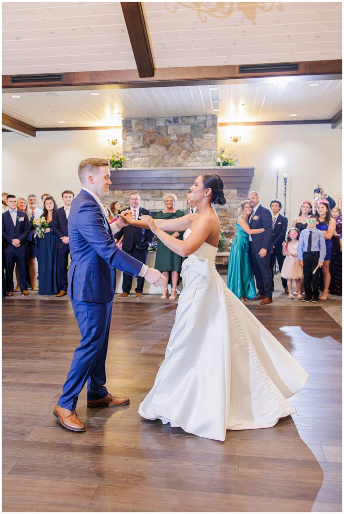 Bride and groom sharing their first dance inside Pembroke Pines Country Club in Pembroke, NH, with guests gathered around a stone fireplace in the background.